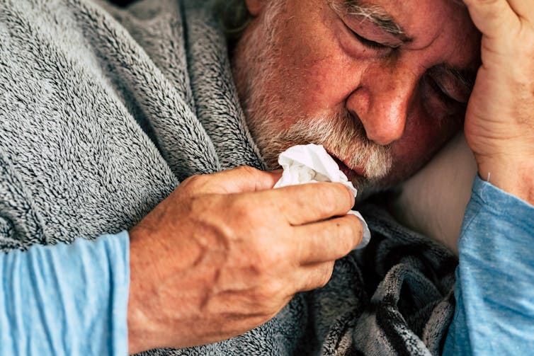 older man sick in bed with tissue