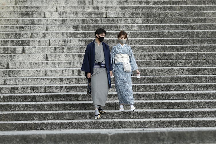 A couple dressed in kimono and wearing protective face masks walk down deserted stairs at Kiyomizu-dera Temple, a popular tourist destination in Japan.