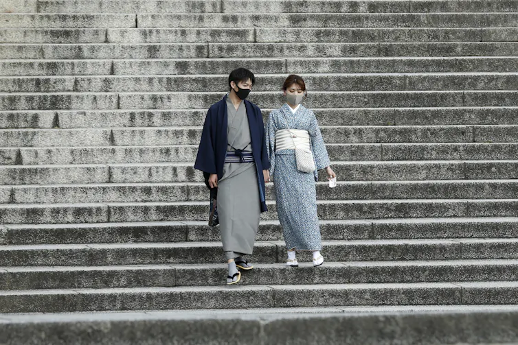 A couple dressed in kimono and wearing protective face masks walk down deserted stairs at Kiyomizu-dera Temple, a popular tourist destination in Japan.