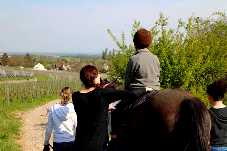Un enfant est installé sur un cheval, dans la nature, assuré par des soignants.