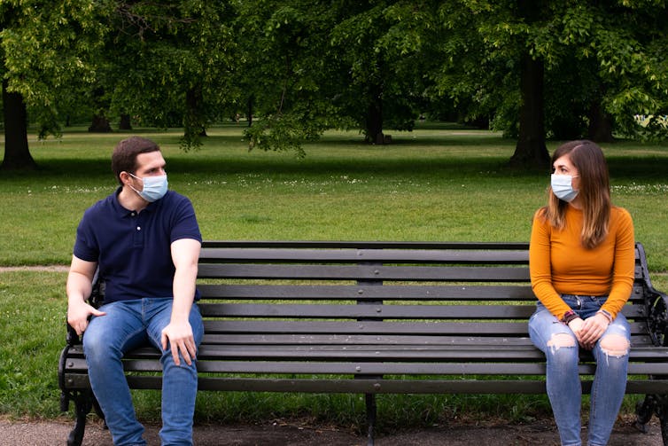 Two people wearing masks sat on park bench
