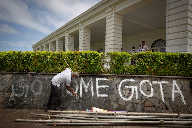 A man washes graffiti saying'Go Home Gota' from a wall.