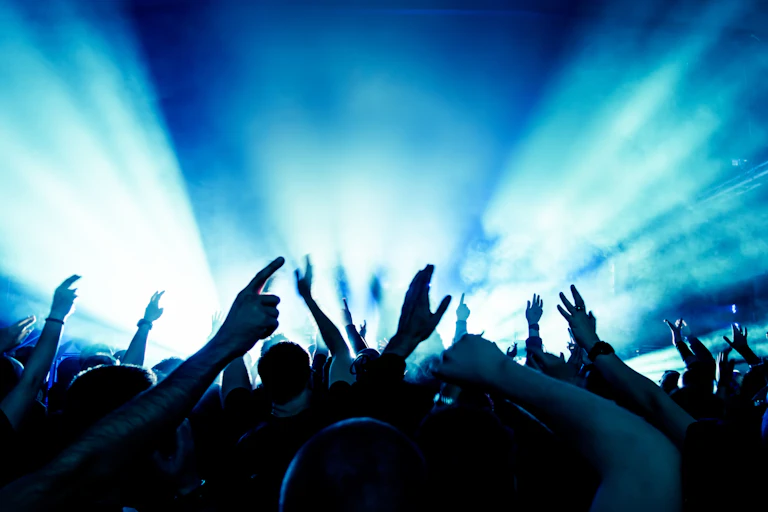 Manos acompasadas ante el escenario de un concierto, todo en tonos azules.