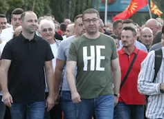 A man in glasses wearing a T-shirt marches in the street.