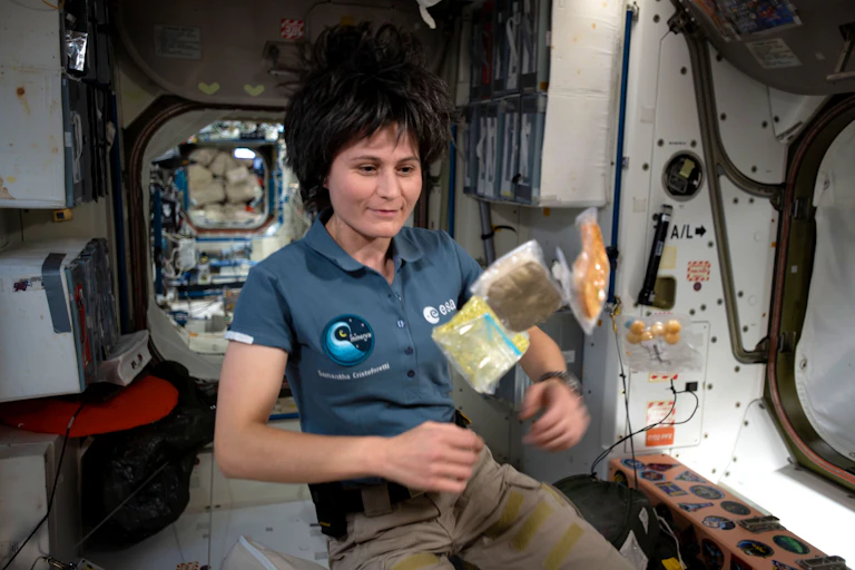 L'astronaute Samantha Cristoforetti flotte dans l'ISS devant trois sachets de nourriture