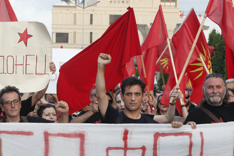 A dark-haired man raises his fist as he marches alongside others waving the Macedonian flag and carrying banners.