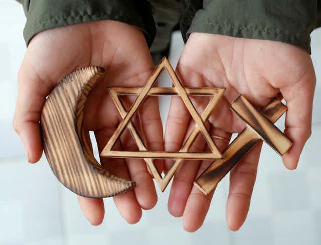 Symboles des trois religions monothéistes  tenus par des mains ouvertes.