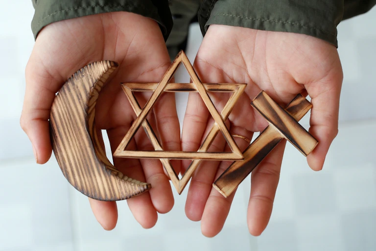 Symboles des trois religions monothéistes tenus par des mains ouvertes.