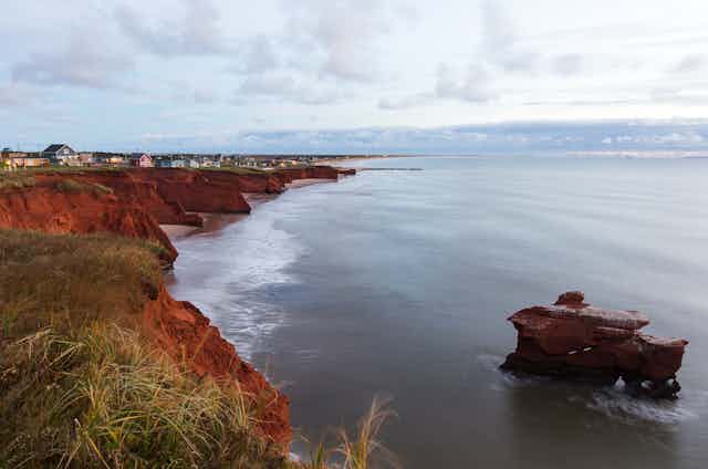 An eroded cliff next to the ocean, with a row of houses perched on top. 