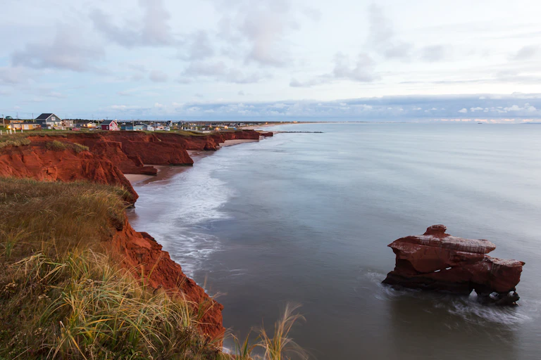 An eroded cliff next to the ocean, with a row of houses perched on top.