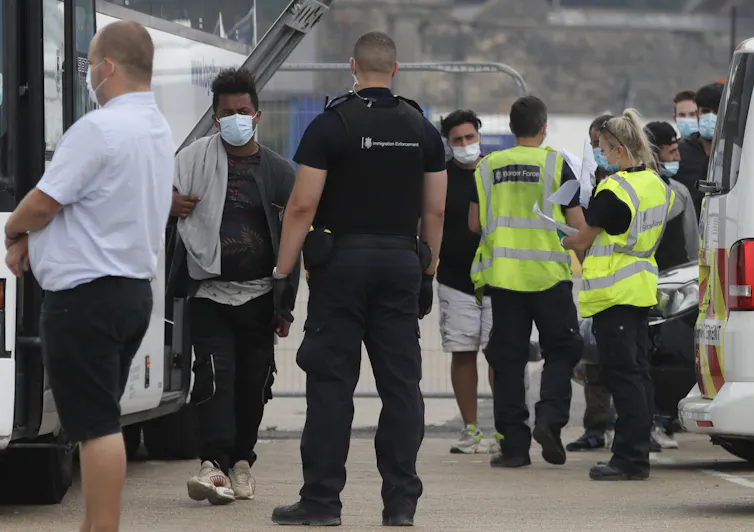 A group of men are escorted by several border force officers in bright yellow vests