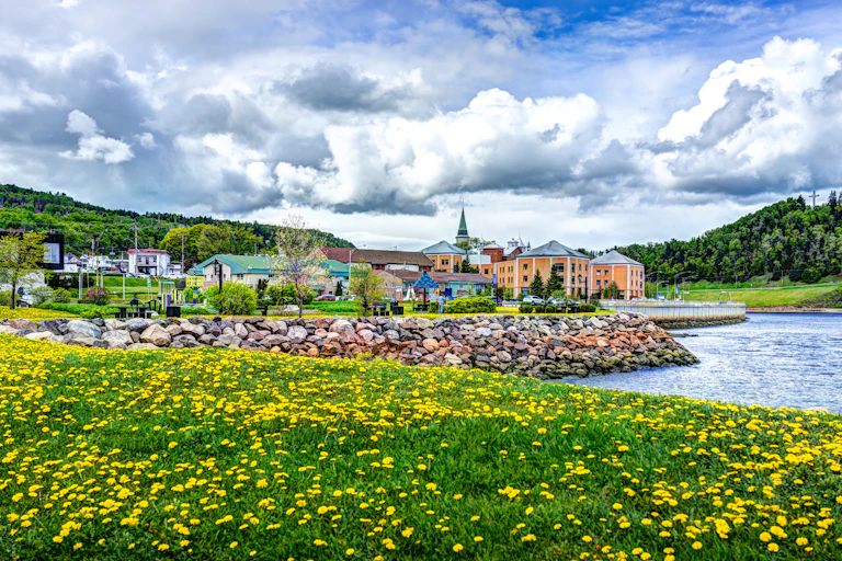 A town sits on the water's edge, reinforced with large stones, under a cloudy sky.