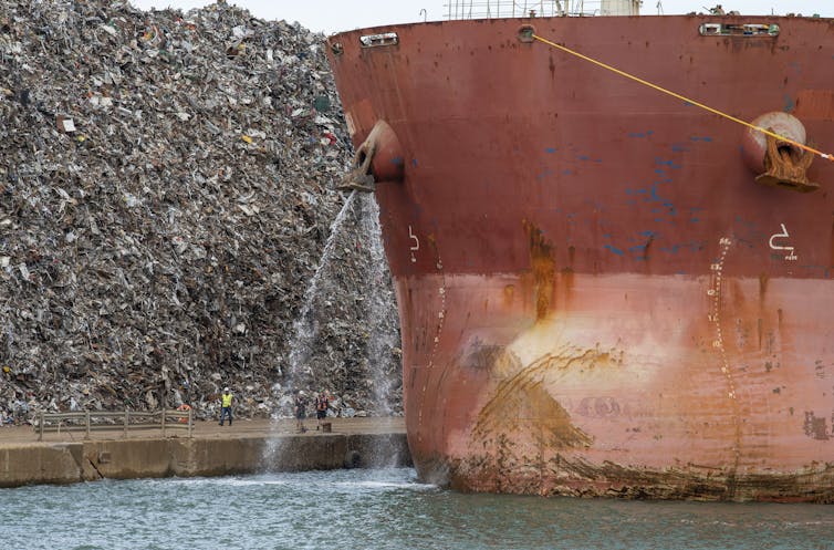 Water pours from an outlet on a large bulk carrier vessel's bow into the harbor.