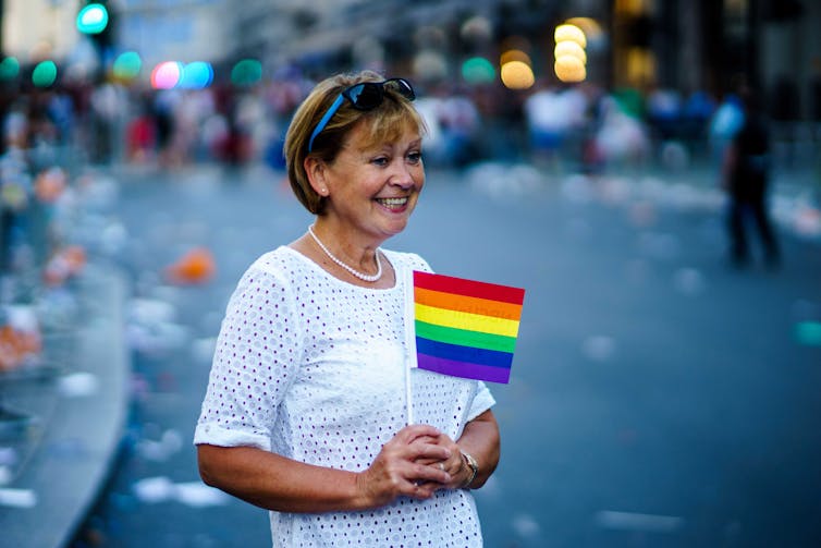 An older white woman holds a Queer flag.