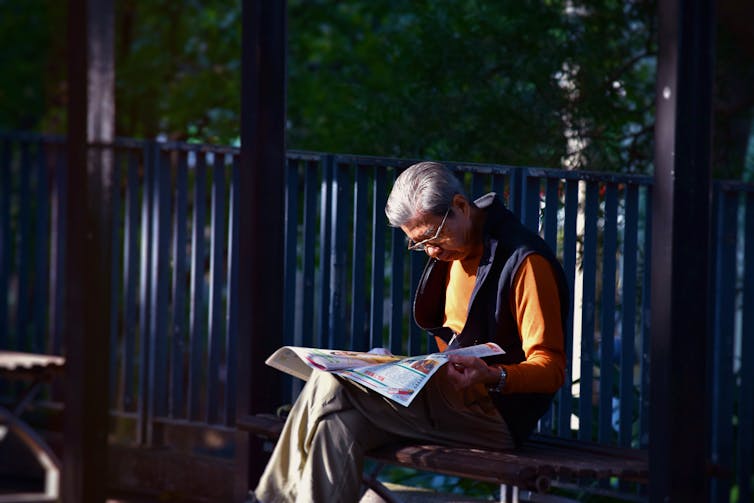 An older Asian man reads a newspaper.