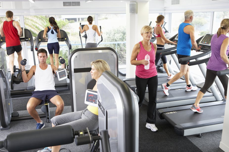 A busy gym full of adults using treadmills, ellipticals and other exercise machines for lifting weights.