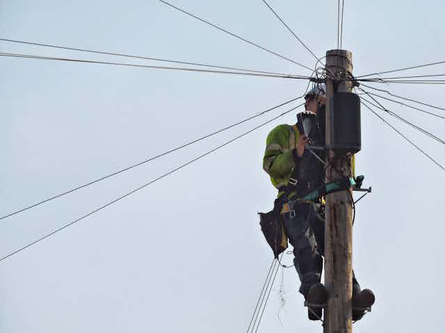 An engineer repairs cables on a telegraph pole.