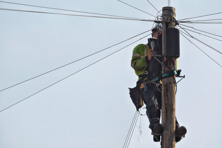 An engineer repairs cables on a telegraph pole.