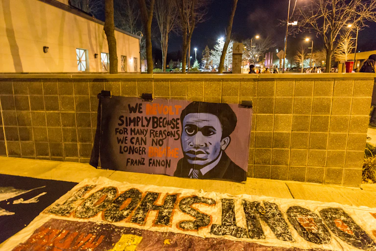A man's face is depicted on a wall with the slogan: We revolt simply because for many reasons, we can no longer breath