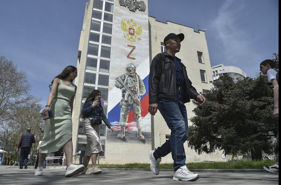 Pedestrians pass a mural depicting a Russian soldier, the Russian flag and double-headed eagle coat of arms as well as the 'Z' military symbol, on the side of a building in Simferopol, Crimea.