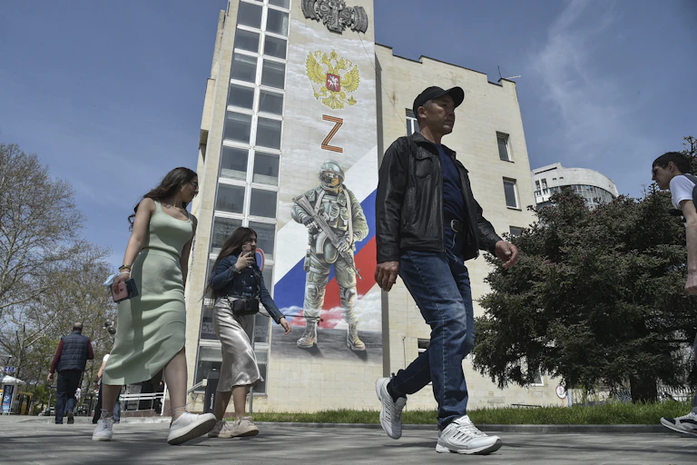 Pedestrians pass a mural depicting a Russian soldier, the Russian flag and double-headed eagle coat of arms as well as the 'Z' military symbol, on the side of a building in Simferopol, Crimea.