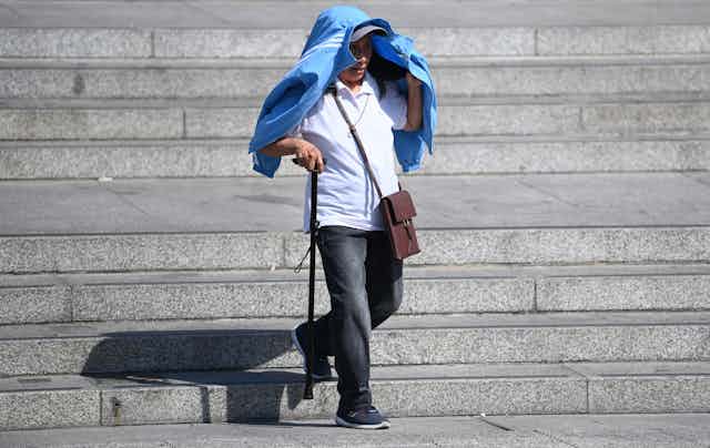 Man with walking stick uses jacket to shelter from sun