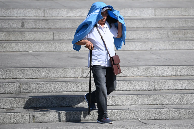 Man with walking stick uses jacket to shelter from sun