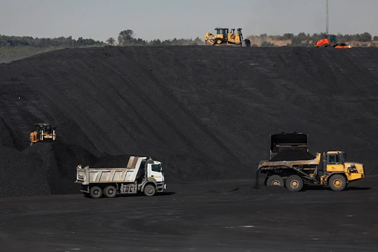 Large trucks against a tall bank of dark material