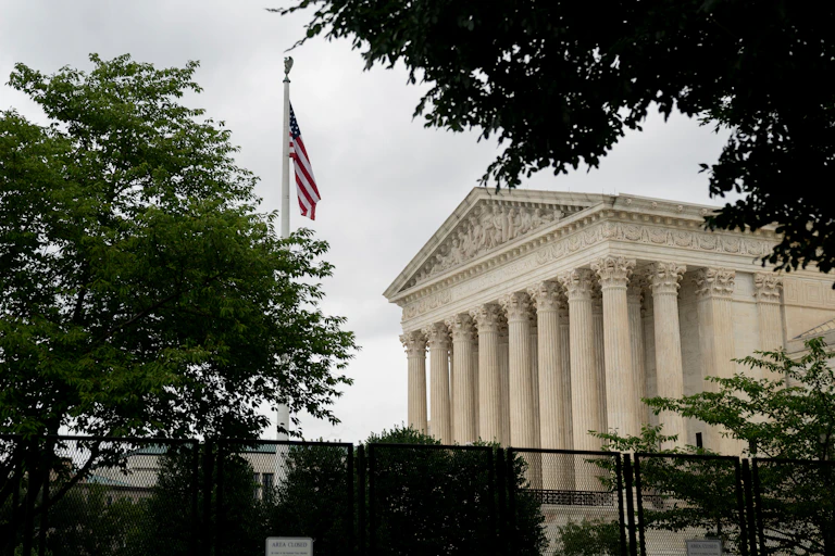 An American flag is seen near a white building with a marble facade designed in the style of classic Roman architecture with giant columns.