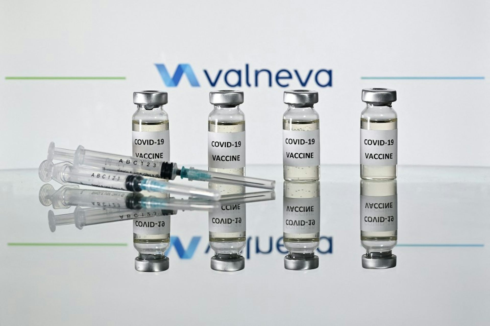 Quatre fioles de vaccins Valneva sont disposées debout derrière une seringue