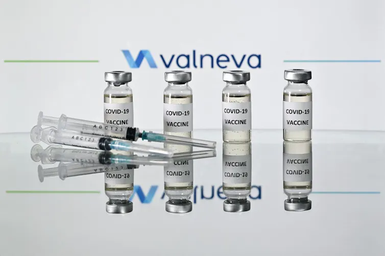Quatre fioles de vaccins Valneva sont disposées debout derrière une seringue