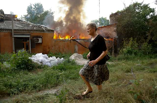 A woman in a black runs past a house that is on fire