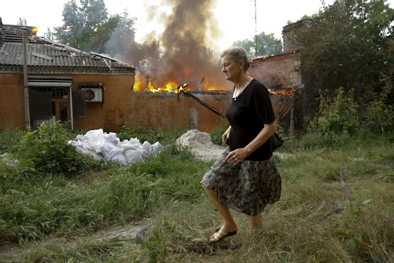 A woman in a black runs past a house that is on fire