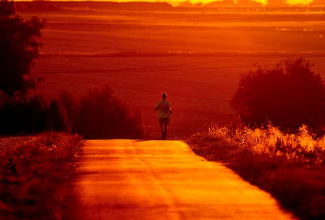 A man runs on a country road bathed in red crimson from the sun