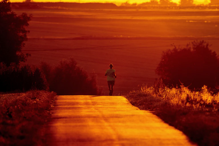 A man runs on a country road bathed in red crimson from the sun
