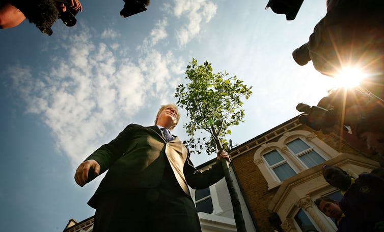 A man holding onto a small tree speaks with reporters.