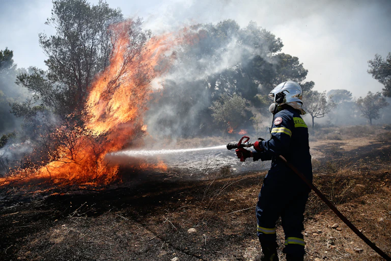 A firefighter douses a bush fire with water.
