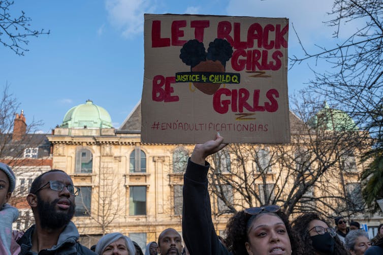 Protestors hold up a poster against a blue sky.