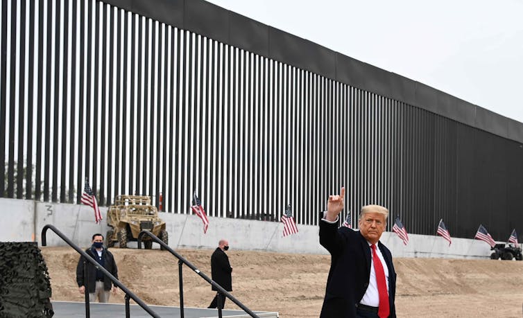 Trump gives a thumbs-up sign in front of a section of newly constructed wall.