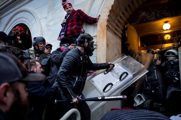 A group of male rioters storm the U.S. Capitol appearing to storm security in dark uniforms