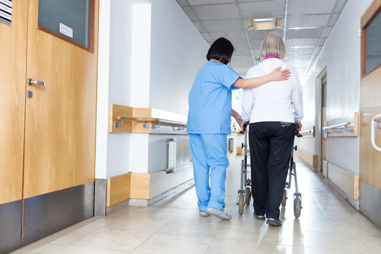 Nurse walking with a patient in a hospital corridor.
