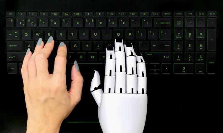 a human hand and a robot hand rest on a keyboard
