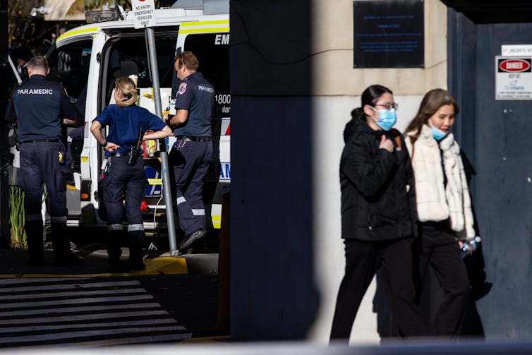 Women in masks walk past paramedics