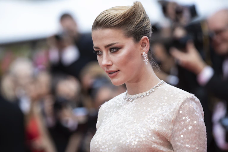 Actress Amber Hears pictured above-waist on a red carpet, in a sparkly white dress and slicked back hair