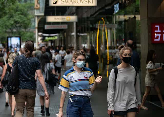 People in masks walk on a busy shopping strip