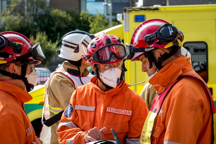 Three members of the fire and rescue services in orange suits, red helmets and face masks