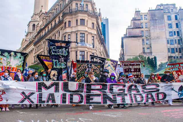 Protestors wearing COVID masks march with colourful banners in a street.