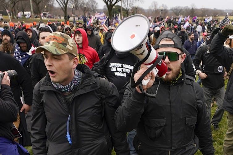 Men in baseball caps walk among a crowd. One carries a megaphone.