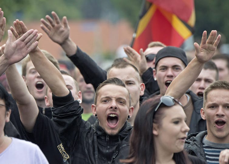 A crowd of angry white people, many with their hands raised.