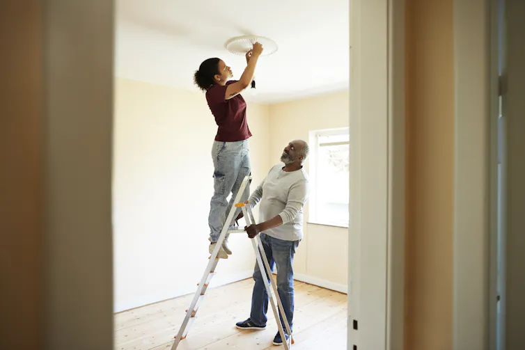 man holds ladder while woman works on ceiling fixture